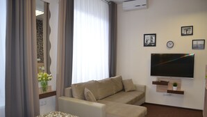 Une chambre d’hôtel avec un lit, un canapé, une télévision et une fenêtre avec des rideaux.