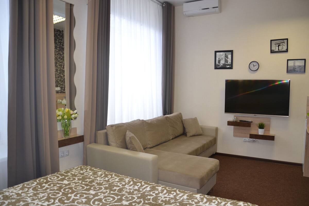 A hotel room with a bed, a sofa, a TV, and a window with curtains.