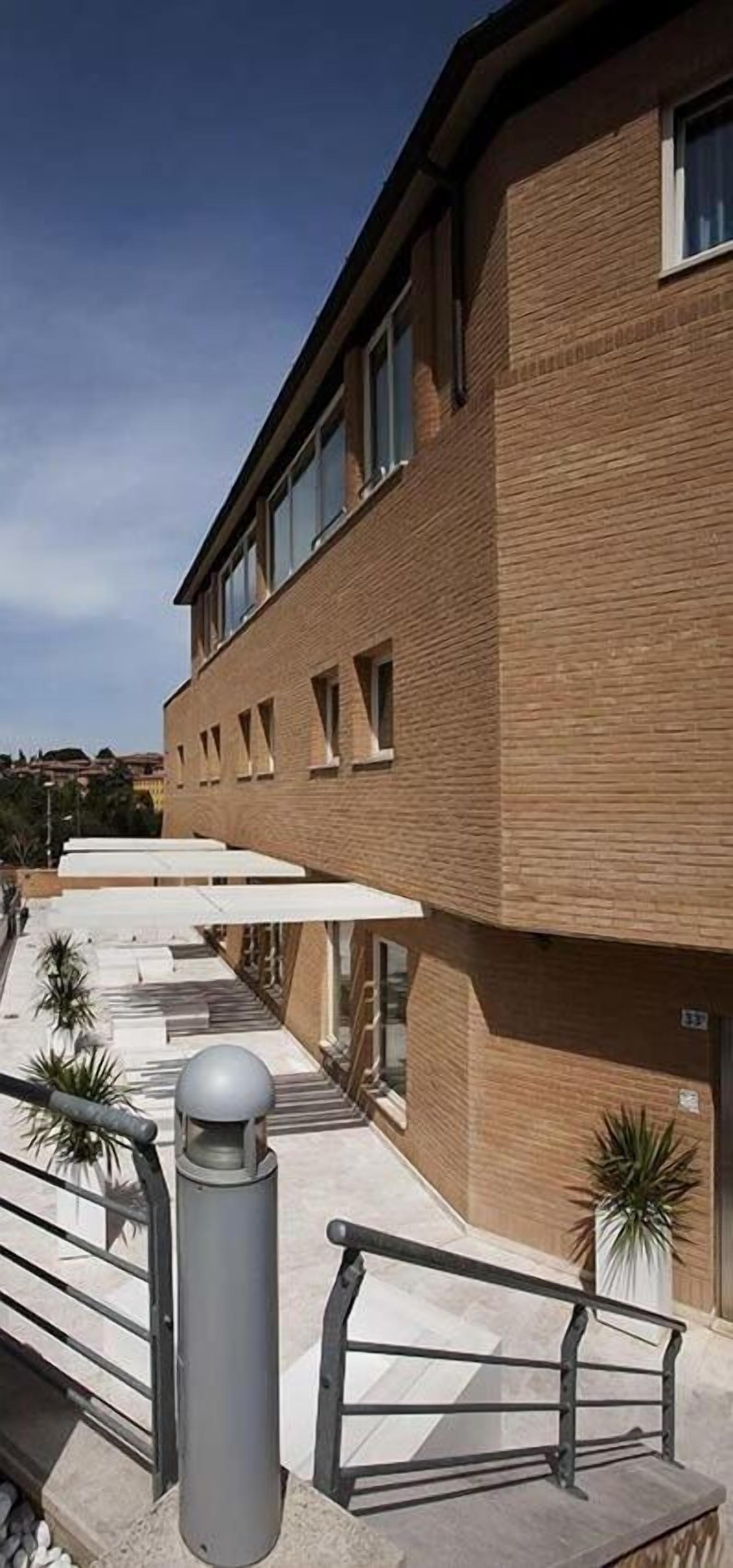 Un bâtiment moderne avec une façade en briques, de grandes fenêtres et un espace extérieur couvert, accessible par un escalier menant à l’entrée.