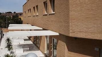Un bâtiment moderne avec une façade en briques, de grandes fenêtres et un espace extérieur couvert, accessible par un escalier menant à l’entrée.