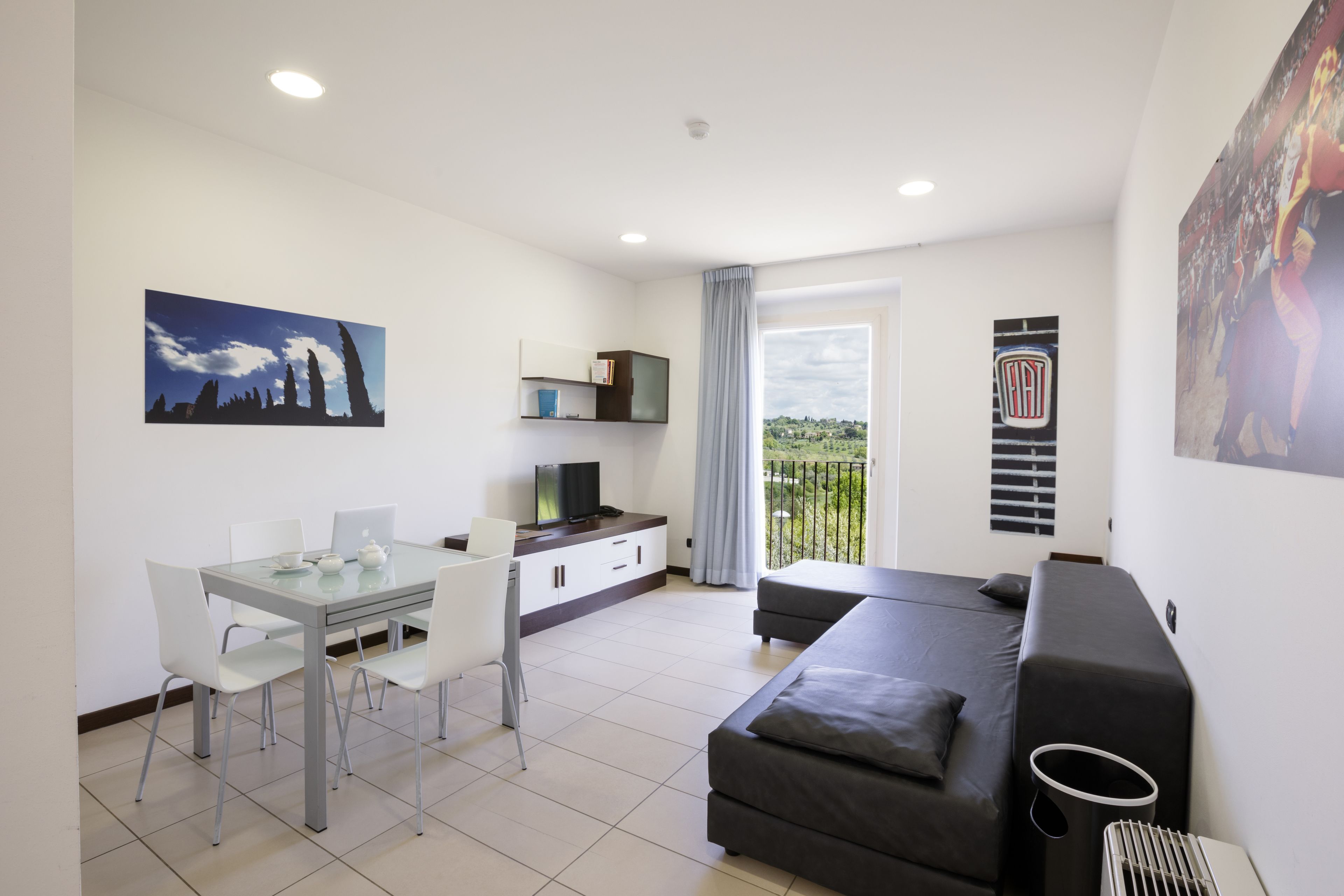 Uma sala de estar moderna com sofá, mesa de jantar com cadeiras, televisão e varanda com vista.