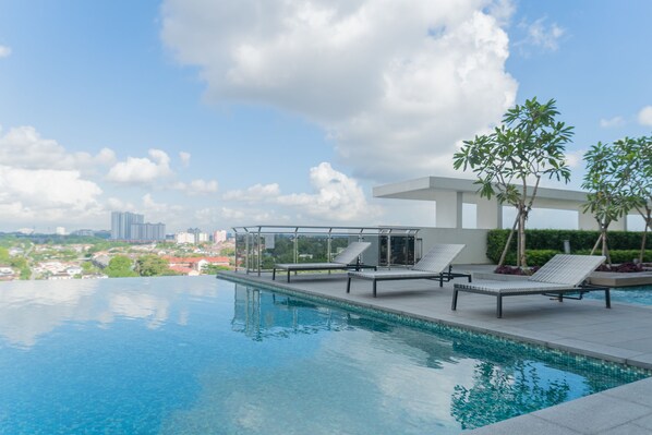 A swimming pool with lounge chairs and a glass-enclosed structure, set against a cityscape.