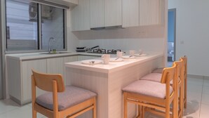 A modern kitchen with a central island, wooden chairs, and a window with blinds.