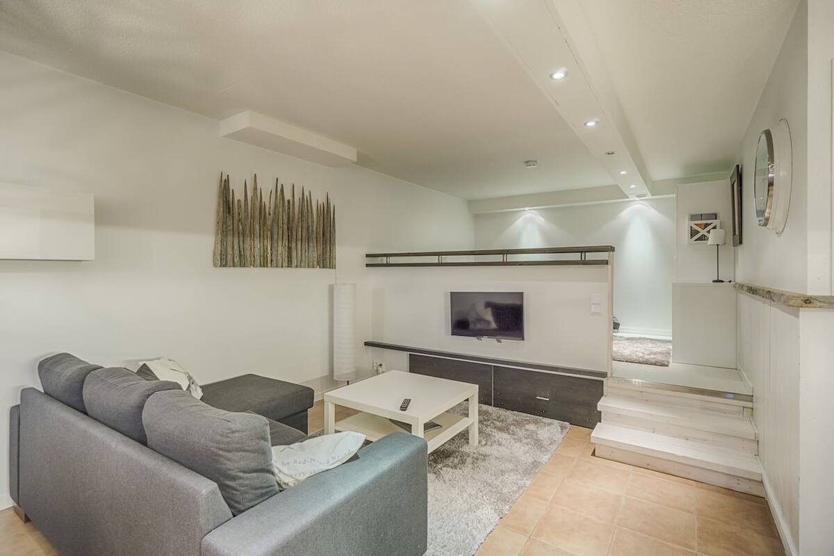 Una sala de estar moderna con un sofá gris, una mesa de centro blanca y un televisor de pantalla plana montado en la pared.