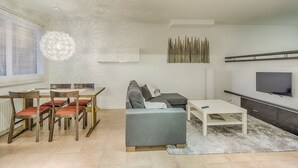 Un soggiorno moderno con divano, tavolo da pranzo, sedie, televisore e lampadario decorativo.