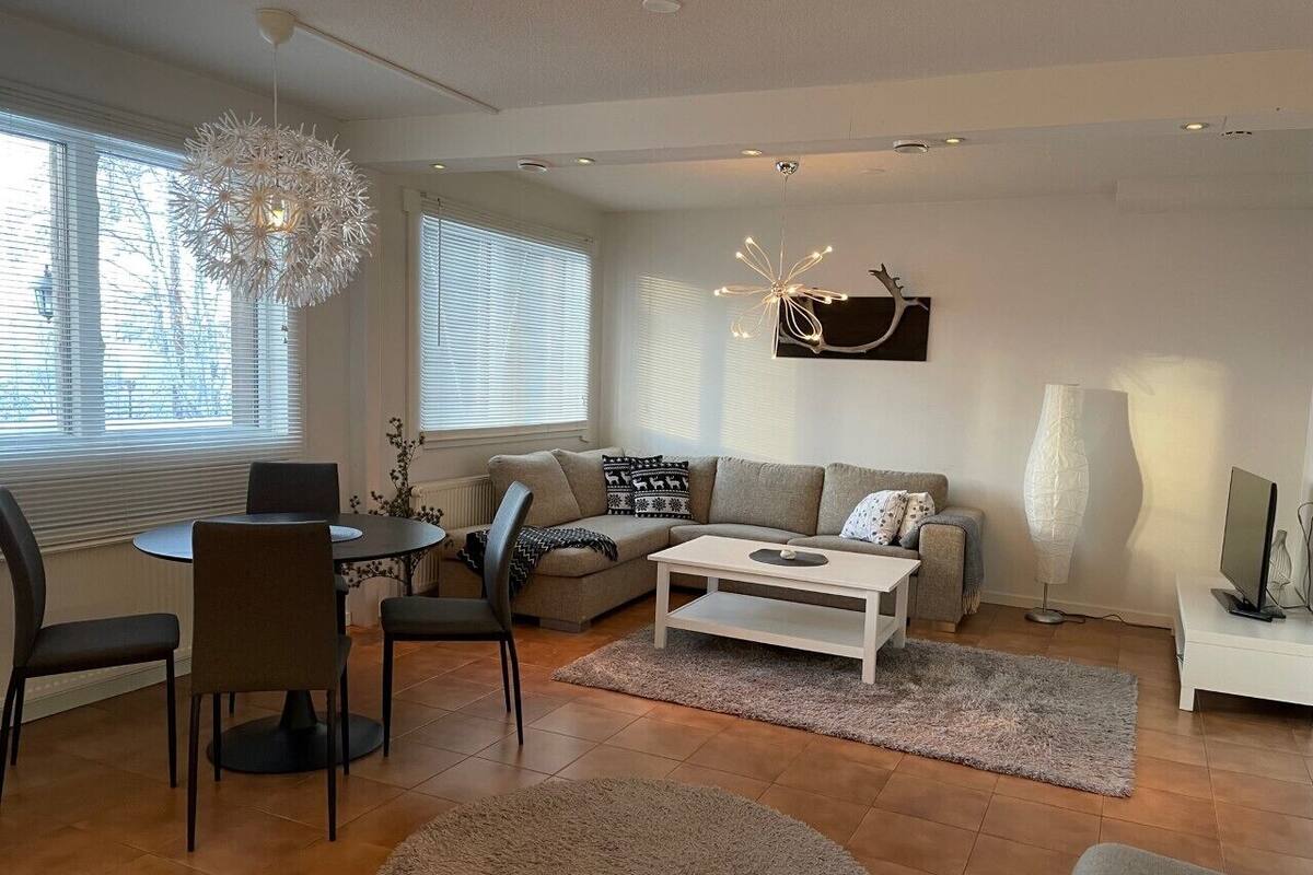 Una sala de estar moderna con una mesa redonda de comedor, dos sofás, una mesa de centro y un gran ventanal con persianas.