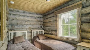 Ein Schlafzimmer in einer Blockhütte mit zwei Betten, einem Fenster mit Blick auf Bäume und einer Holzbalkendecke.