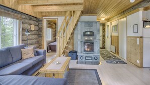 Ein Blockhaus-Interieur mit Kamin aus Stein, Holzbalken, einer Couch und einem Esstisch.