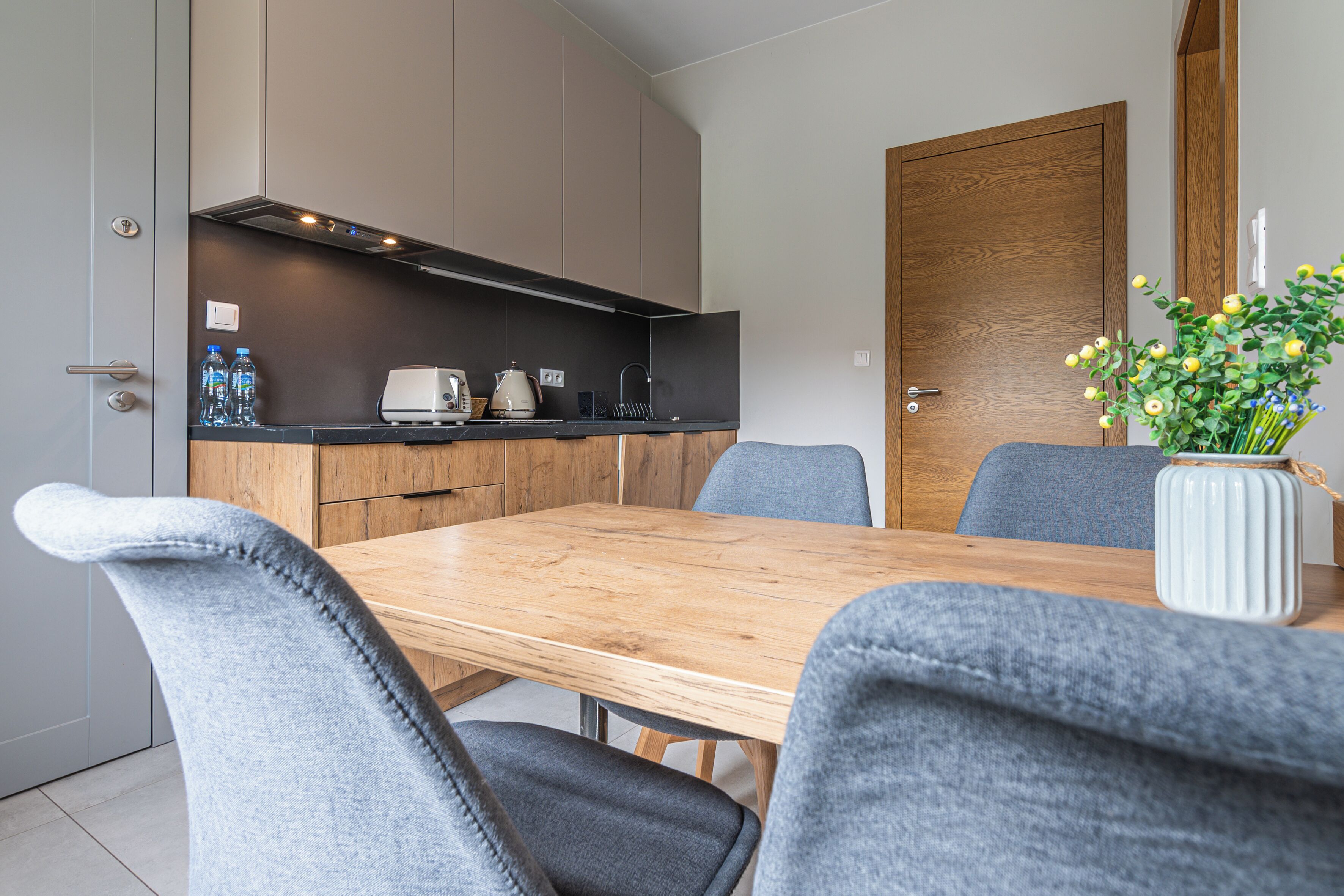A modern kitchen with a wooden table and grey upholstered chairs.