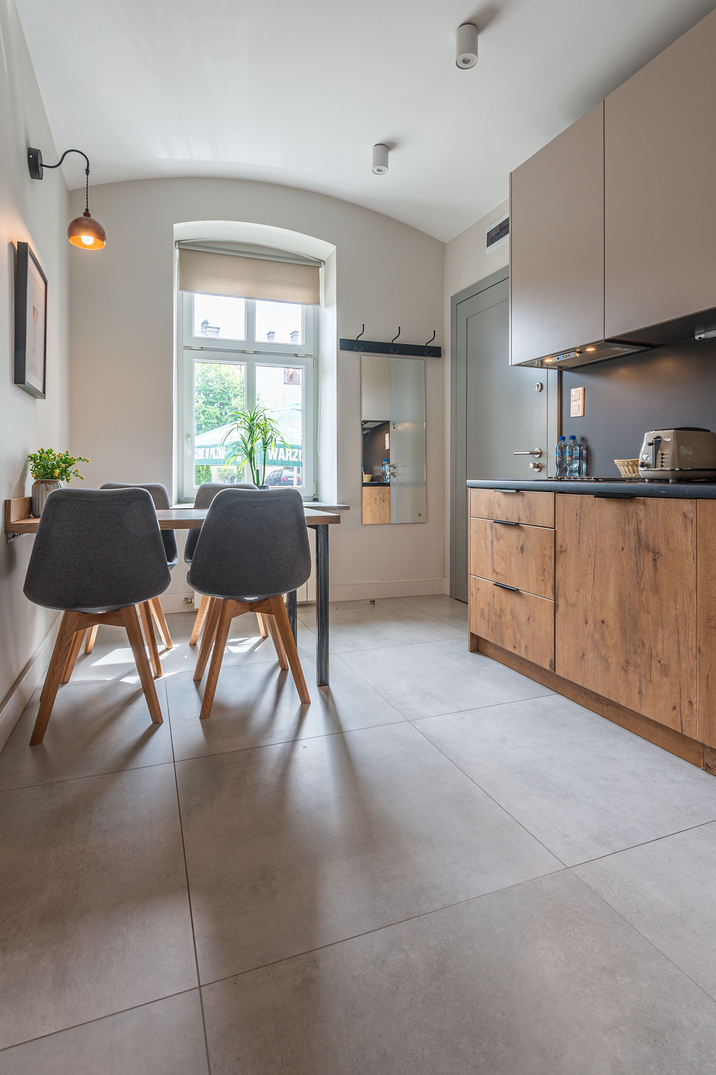 Een moderne keuken met een eethoek, met een groot raam, houten kasten en een betegelde vloer.