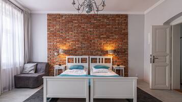 Un dormitorio con pared de ladrillo, una araña, una cama con ropa de cama blanca, una silla y una mesita de noche con lámpara.