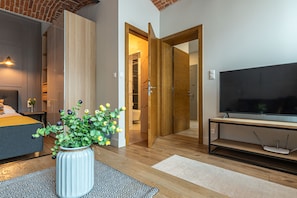 A modern hotel room with a bed, a TV, a wooden floor, and a bathroom visible through an open door. - Staypolska (Oswiecim)