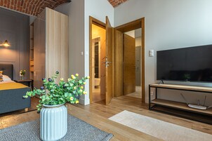 Quarto de hotel moderno com cama, televisão, piso de madeira e banheiro visível através de uma porta aberta.