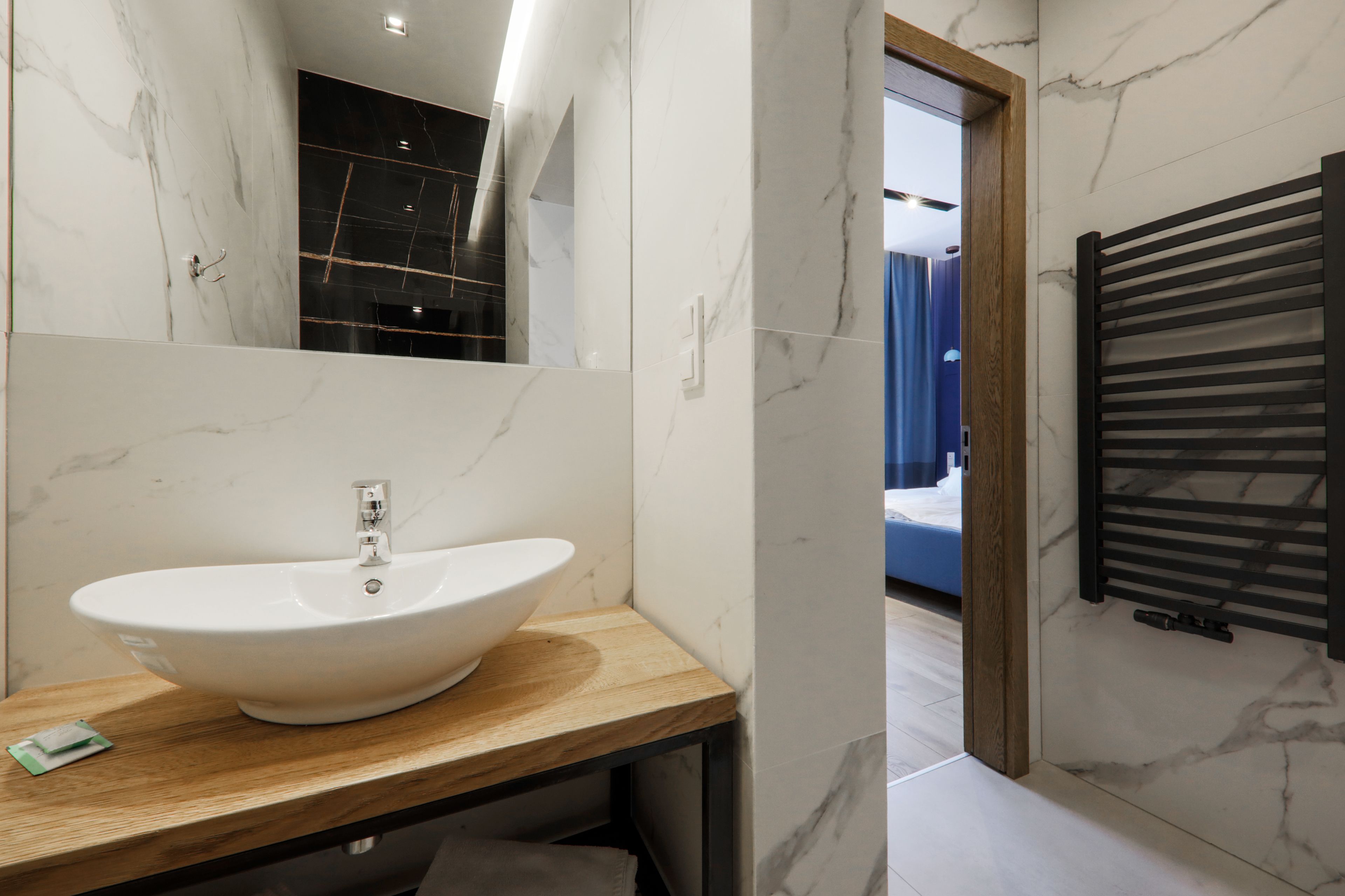 Une salle de bain avec un lavabo en marbre blanc, un plan de toilette en bois et un porte-serviettes noir.