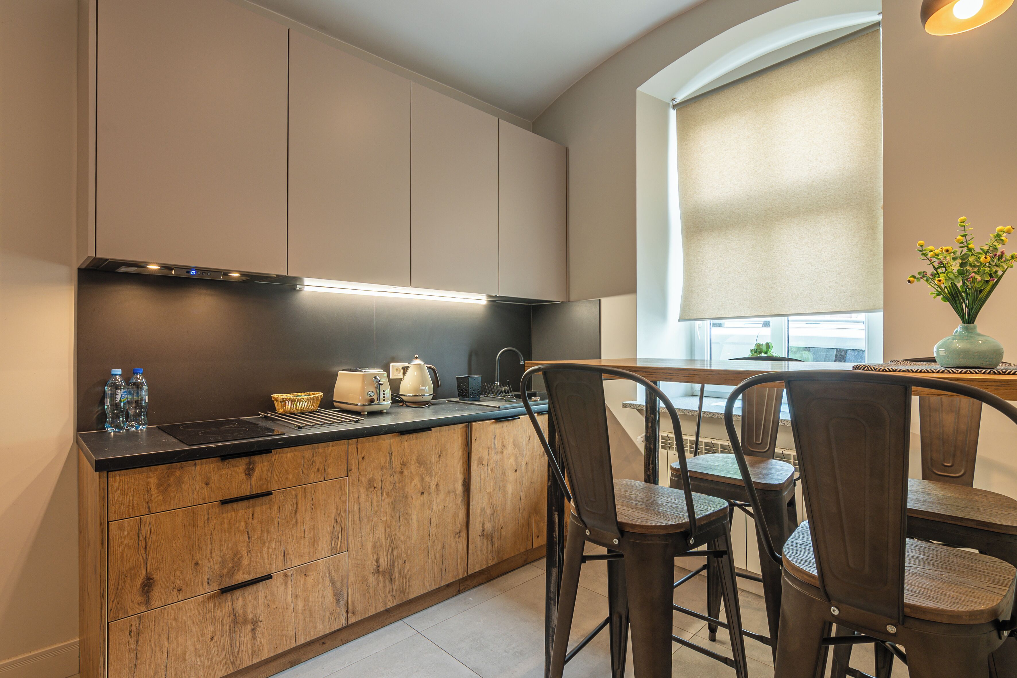 A modern kitchen with wooden cabinets, a black countertop, and a dining area with a table and chairs.
