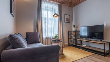 Ein modernes Wohnzimmer mit einem grauen Sofa, einem Fernseher auf einem Holzgestell und einer Ziegeldecke.