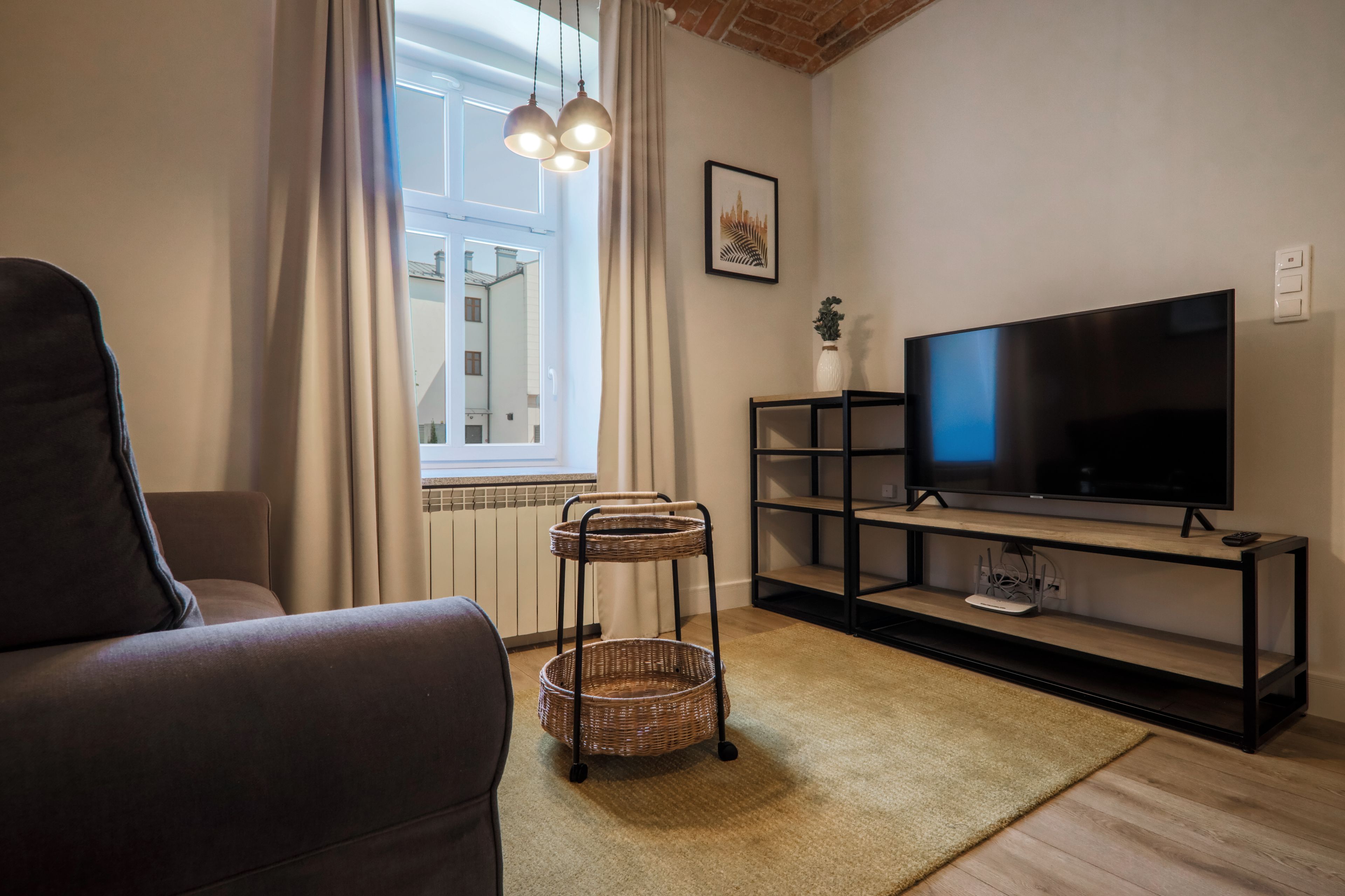Ett vardagsrum med en soffa, en tv på ett tv-bord, ett sidobord i rotting och ett fönster med gardiner.