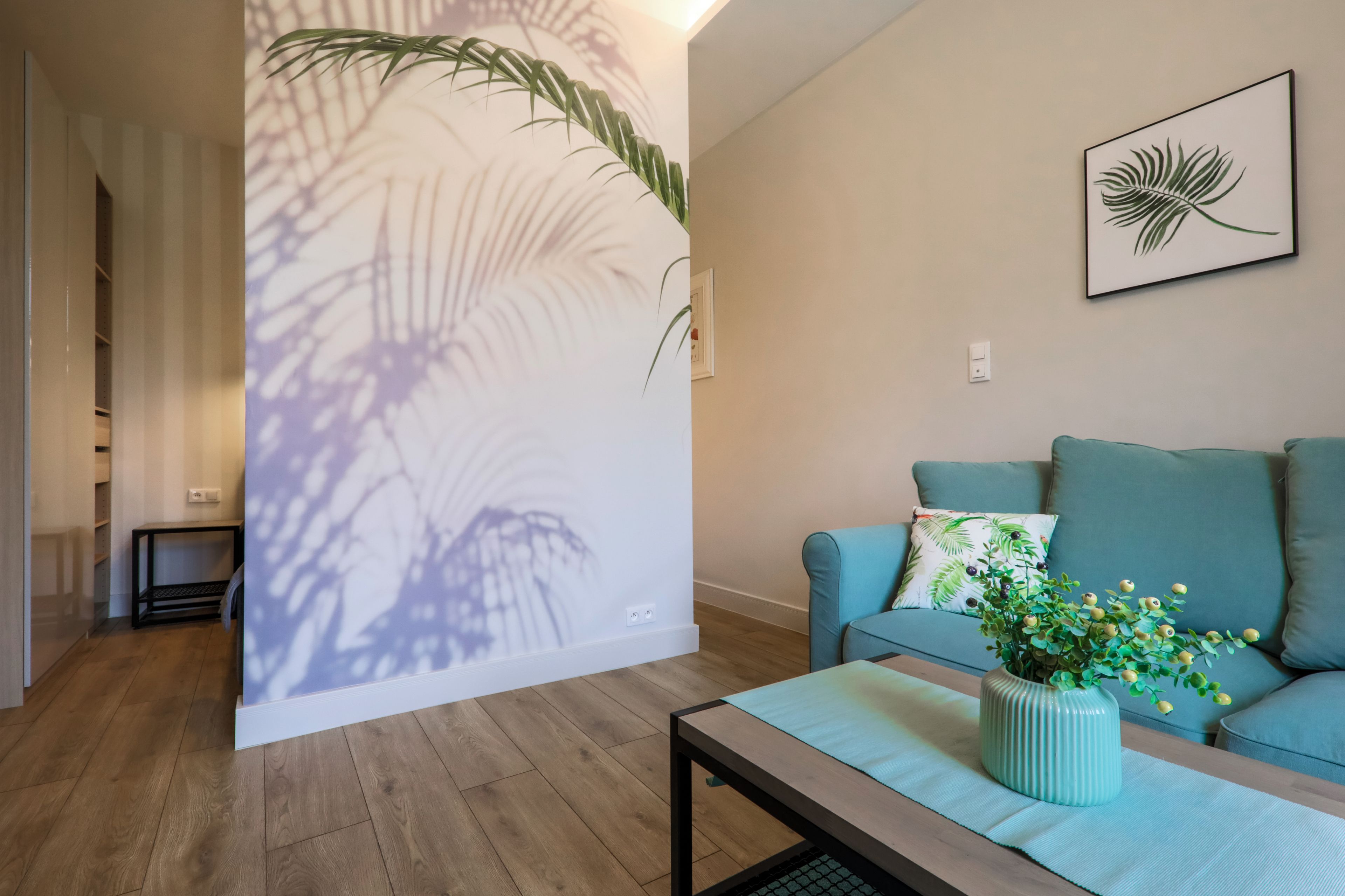 Un salon avec un canapé, une table basse ornée d’un vase et un mur décoré d’un motif de feuilles.