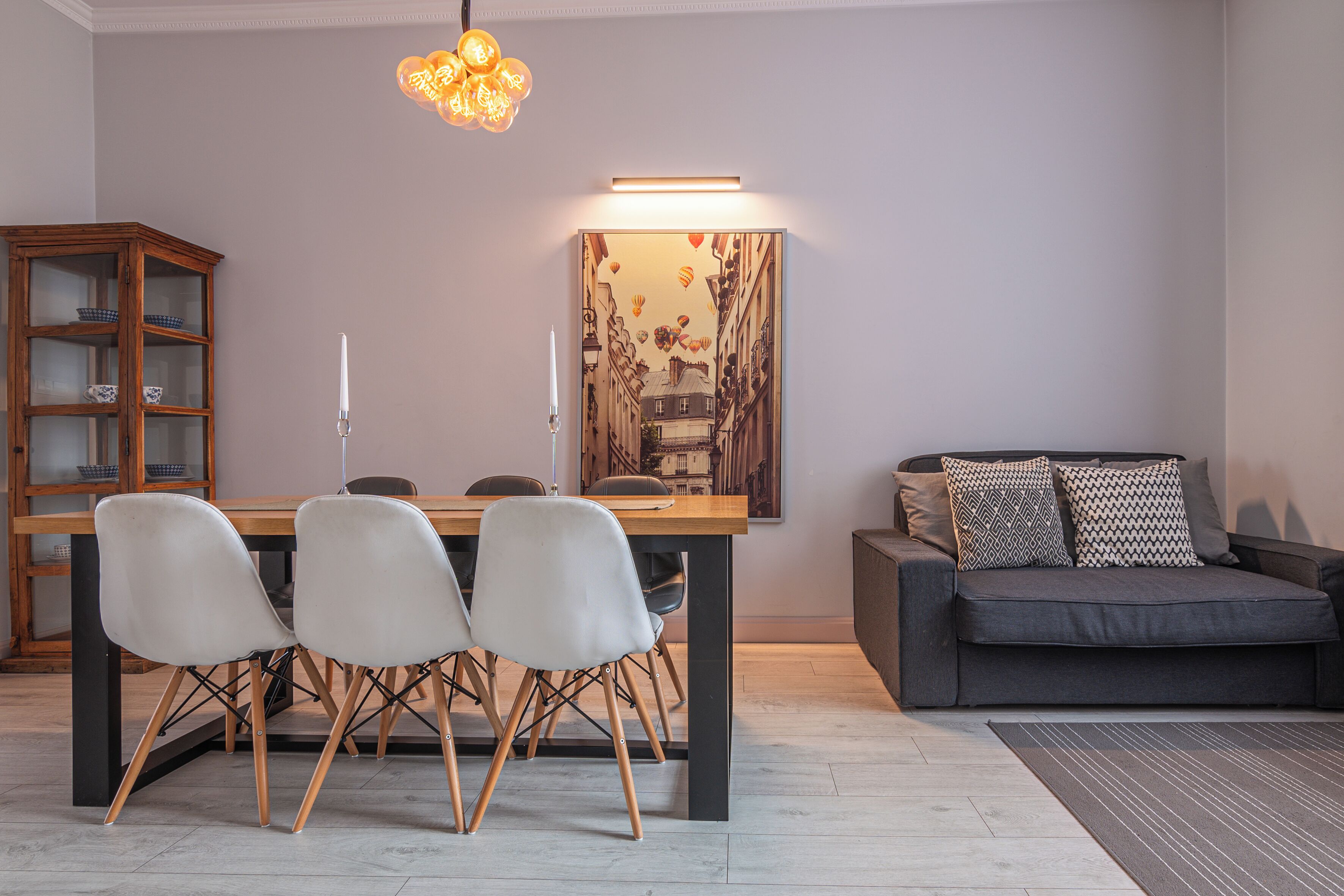 Uma sala de jantar com mesa e cadeiras de madeira, um sofá e uma obra de arte na parede.