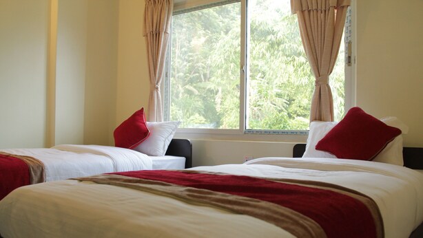 A hotel room with two beds, each with white bedding and red pillows. There is a window with curtains, and the room has a neutral color scheme. - Hotel Brothers Inn (Pokhara)