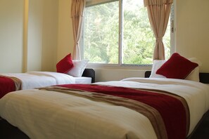 Une chambre d’hôtel avec deux lits, chacun doté de draps blancs et d’oreillers rouges. Il y a une fenêtre avec des rideaux, et la chambre est décorée dans des tons neutres.