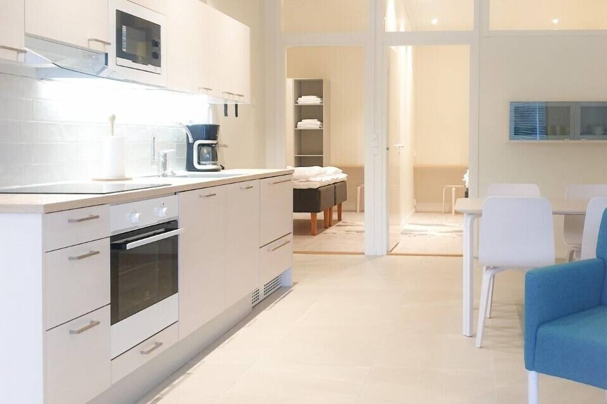 A modern kitchen with white cabinetry, a built-in oven, and a microwave. There is a dining area with a white table and chairs, and a blue chair.