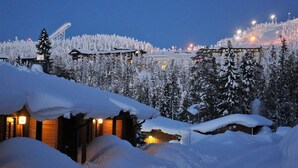 Un albergue cubierto de nieve con varias construcciones, un telesilla y un fondo de bosque.