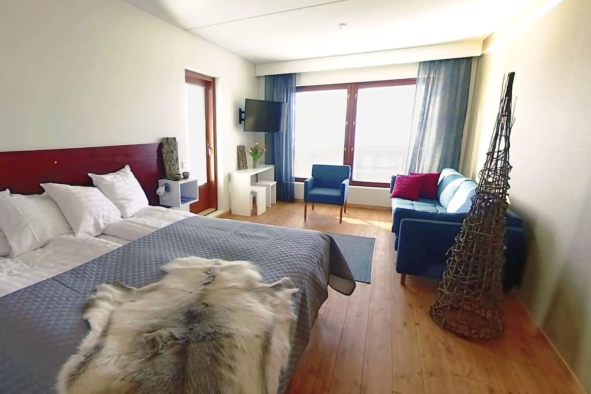 A hotel room with a large bed, a desk, a chair, and a sofa.