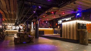 A bar area with wooden tables and stools, a counter with a neon sign, and a wall decorated with photos and star-shaped lights. - Hotel Arctic Zone (Kuusamo)
