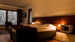 A bedroom with a large bed, a TV mounted on the wall, and a window with blinds. - Hotel Arctic Zone (Kuusamo)