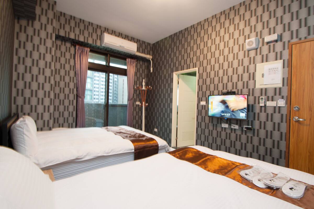 A hotel room with two beds, a television, an air conditioning unit, and a patterned wall.
