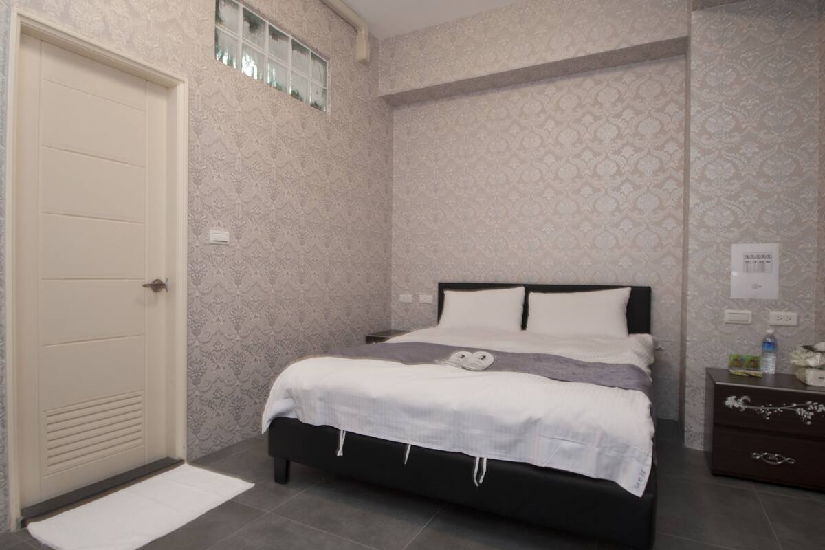 A bedroom with a bed, a nightstand, a dresser, and a door.
