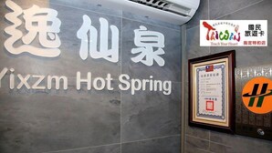 A hotel sign with the name 'Vixzm Hot Spring' and a logo. There is a framed certificate on the wall and a sign with a colorful logo and text. - Yixiang Spring Travel (Jiaoxi)