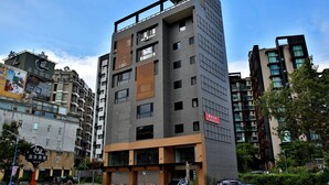 A multi-story hotel with a modern design, featuring a mix of glass and brick facades, and a prominent wooden slat design on one side. - Yixiang Spring Travel (Jiaoxi)