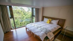 A bedroom with a large bed, a glass table, and a view of greenery through the window. - Yixiang Spring Travel (Jiaoxi)