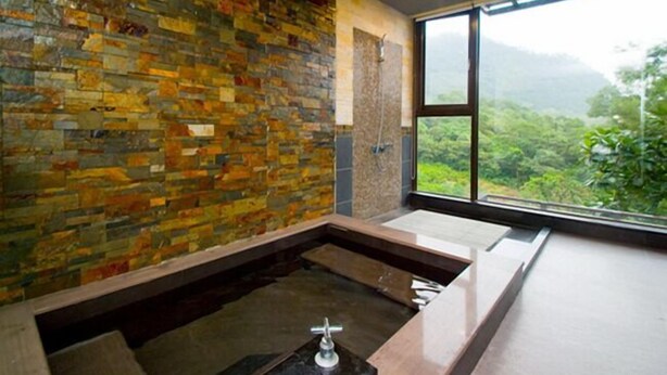 A modern bathroom with a stone wall, a large window, and a bathtub. - Yixiang Spring Travel (Jiaoxi)