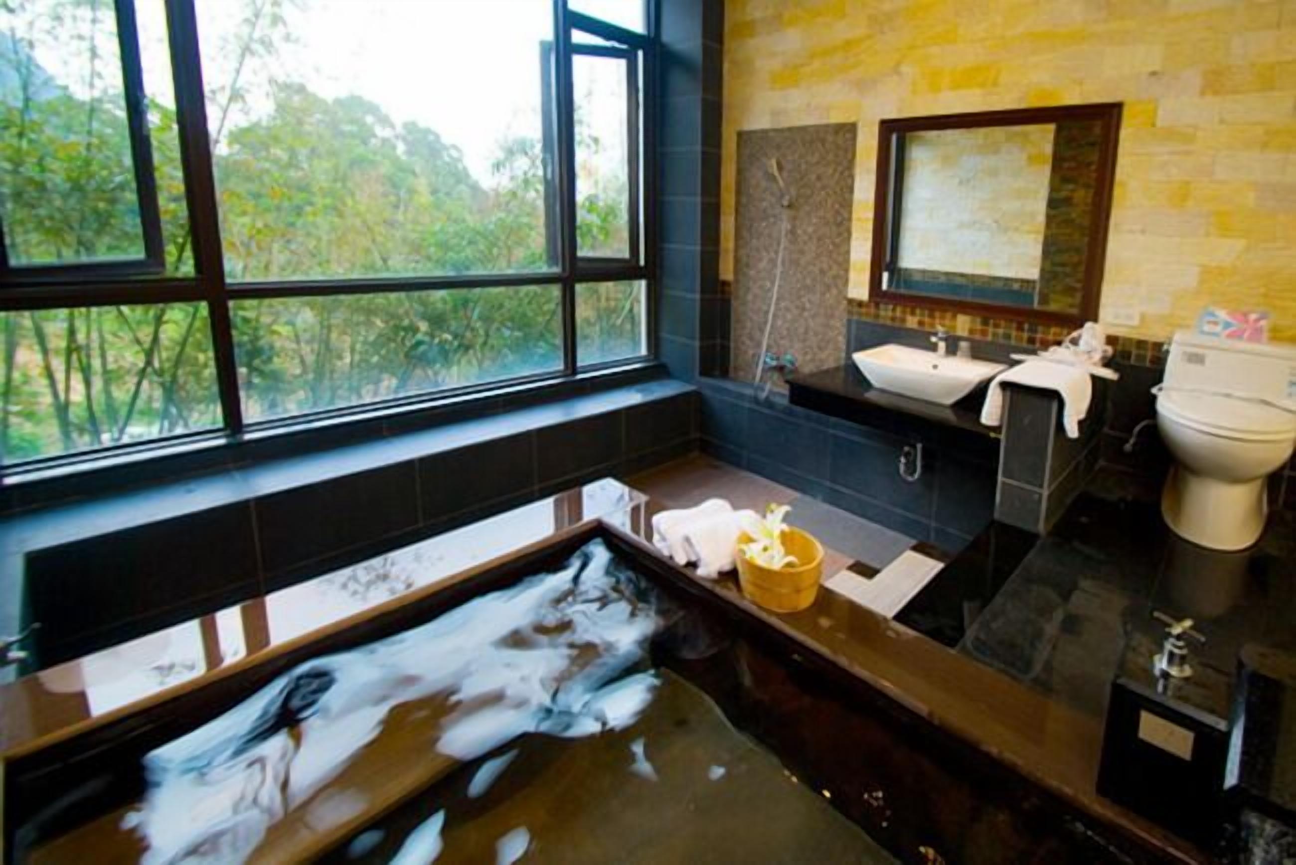 Ein Badezimmer mit großem Fenster, einer Badewanne voller Schaum, einem Waschbecken und einer Toilette.