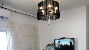 Un salon avec un canapé, une plante en pot, un téléviseur et un petit meuble.