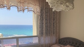 Une chambre à coucher avec un lit, une fenêtre avec des rideaux, un luminaire suspendu et une vue sur la mer.