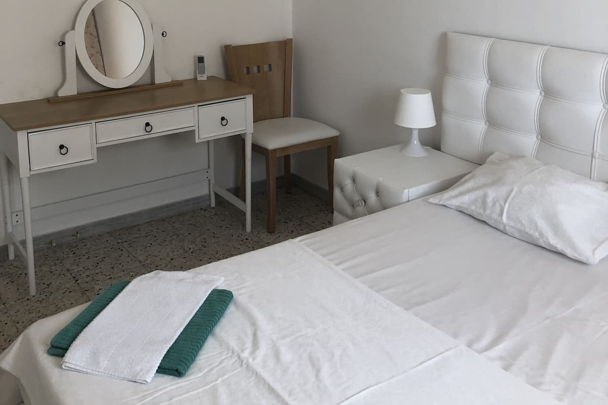Quarto com cama, mesa de cabeceira com abajur, cômoda com espelho, cadeira e pintura de orquídea na parede.