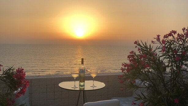 Une vue sur le coucher de soleil depuis une terrasse, avec une table, deux chaises et une plante en pot.