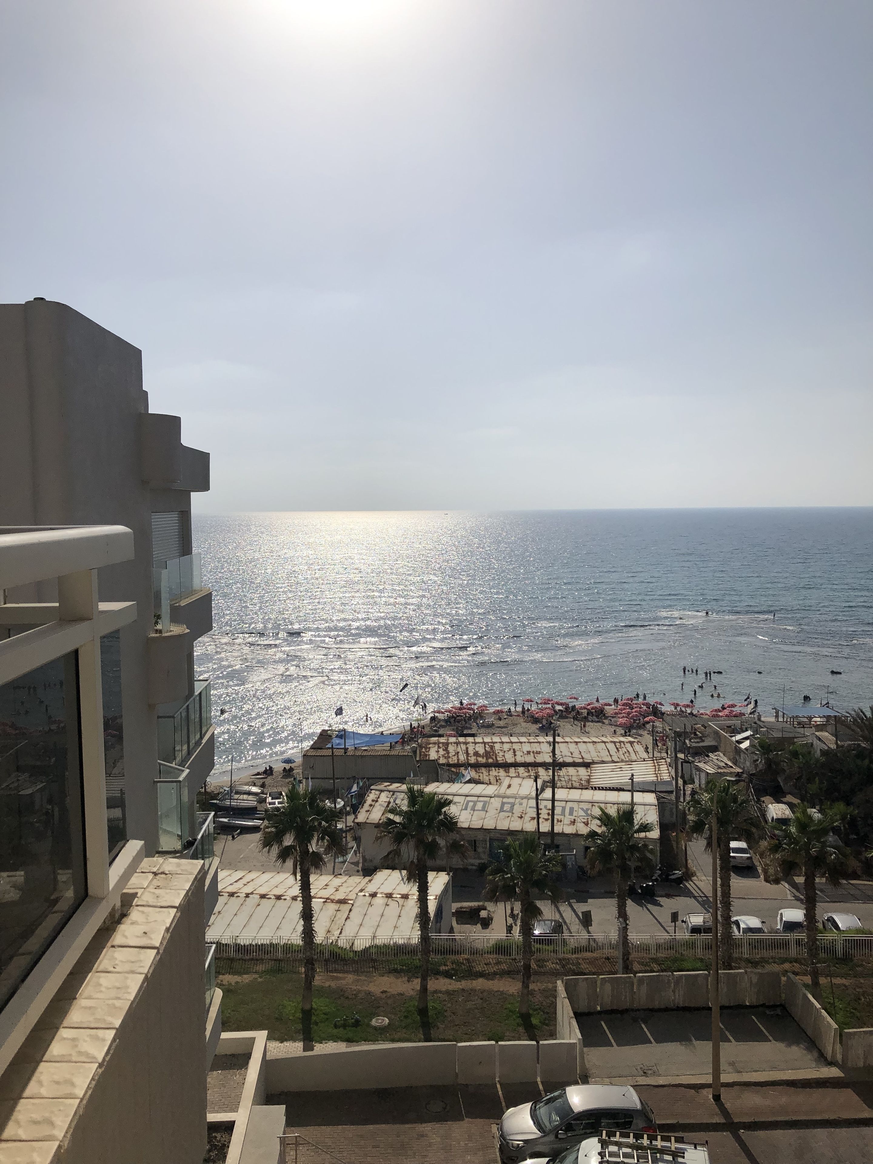 A view of a beach with a parking area and buildings in the foreground.