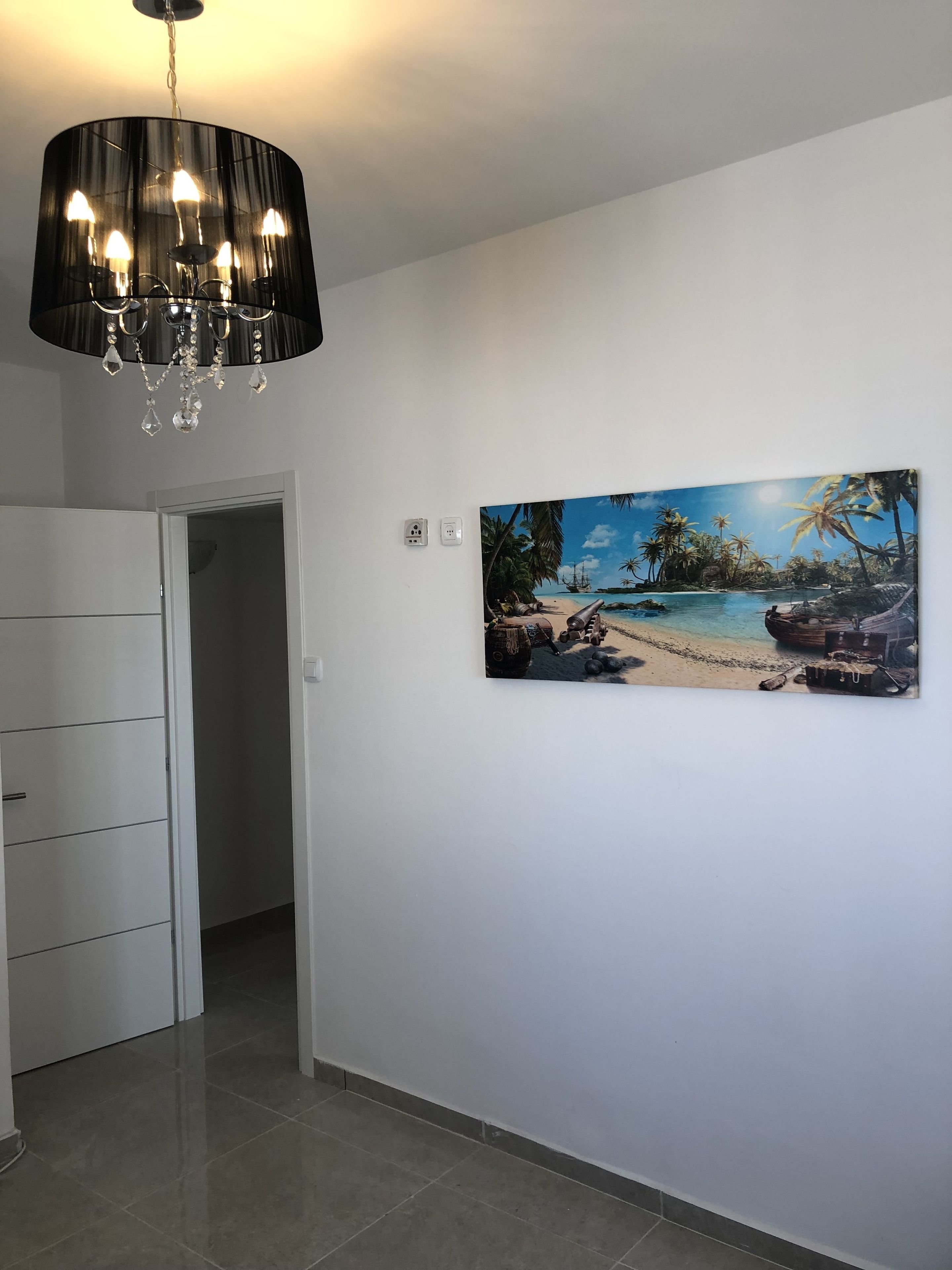 Un corridoio con un lampadario moderno, un armadio bianco e un quadro a tema spiaggia.