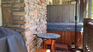 Un'area patio con un muro in pietra, una zona relax coperta con tavolo e sedie, e un ombrellone rosso che offre ombra.