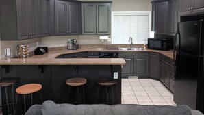 A modern kitchen with dark cabinets, a granite countertop, a built-in microwave, and a refrigerator. There are three stools at the island. - Perfect destination for summer fun and winter sports! (Huntsville)