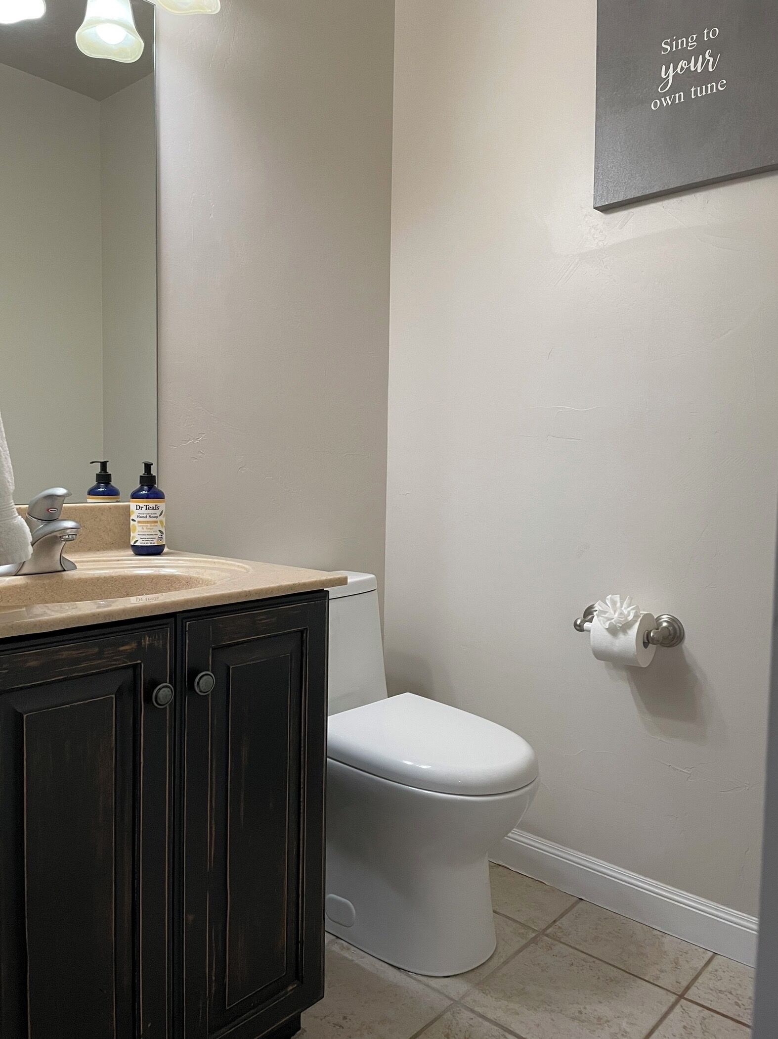 A bathroom with a toilet, a sink with a mirror, and a wall-mounted toilet paper holder.