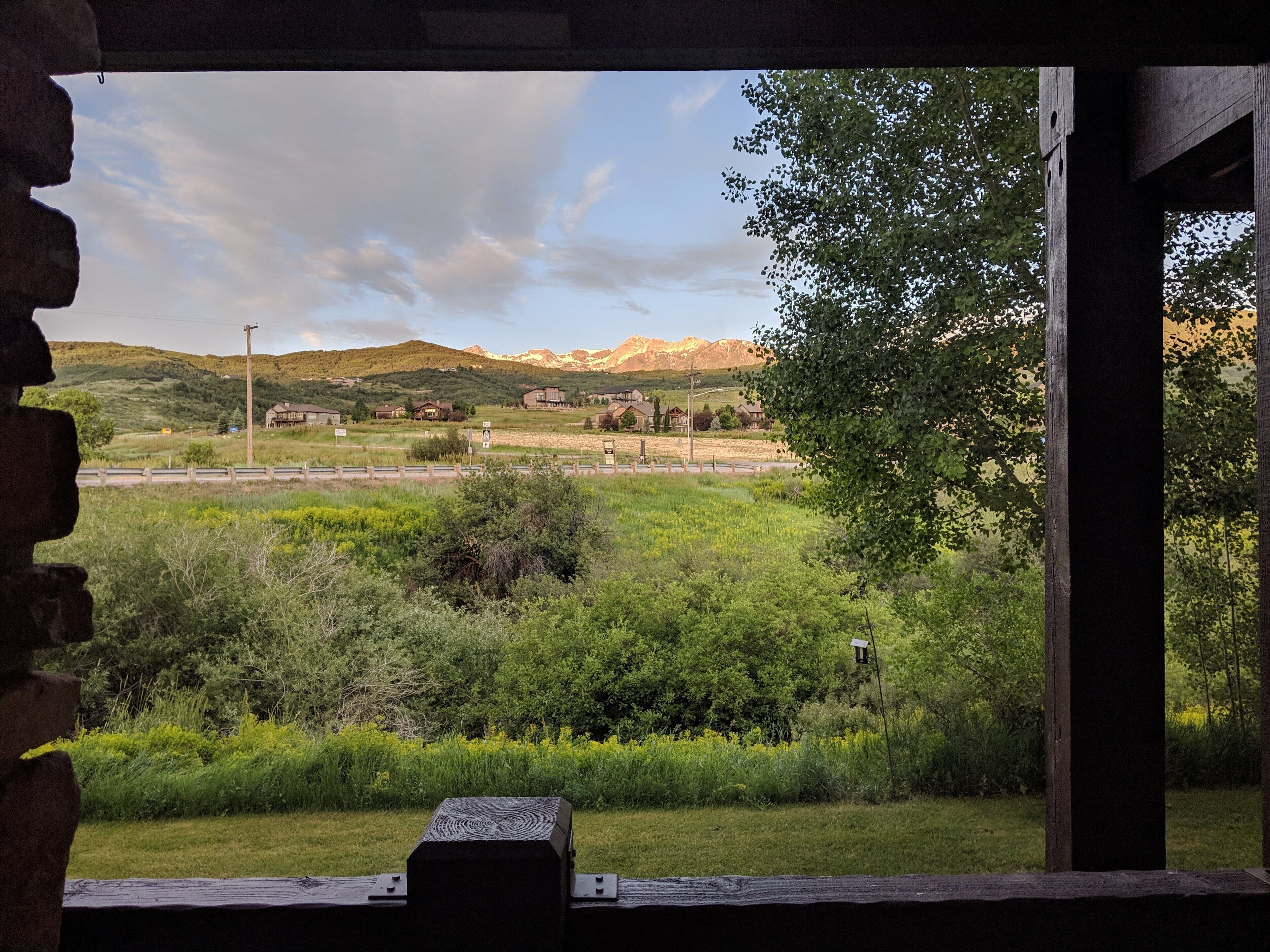 Vista desde una ventana sobre un paisaje rural con montañas a lo lejos, un banco de madera en primer plano y cielo despejado.
