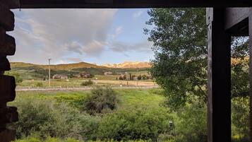 Vista desde una ventana sobre un paisaje rural con montañas a lo lejos, un banco de madera en primer plano y cielo despejado.