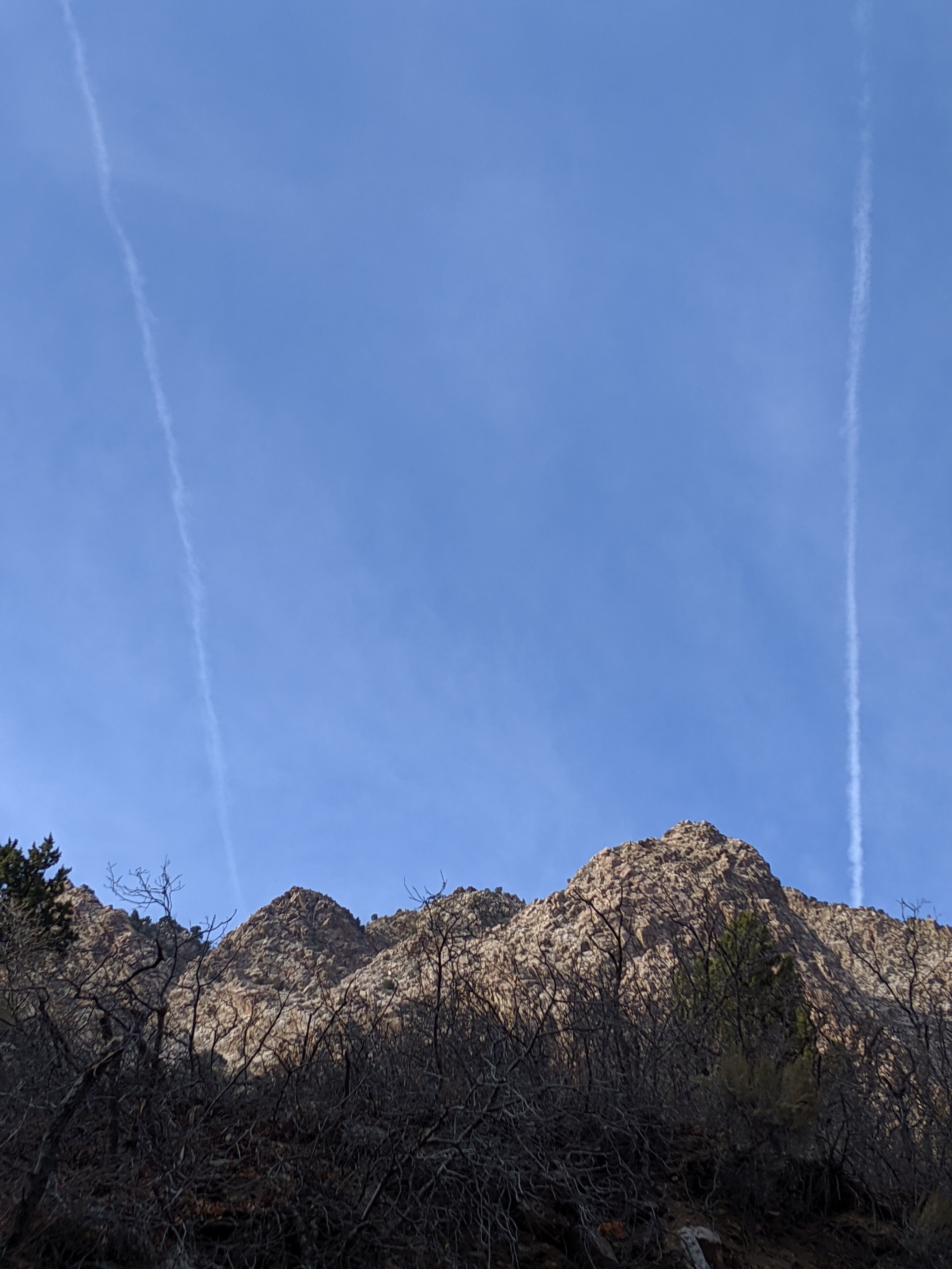 A mountainous landscape with clear skies and two visible contrails.