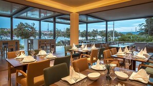 Un restaurante con mesas dispuestas para comer, ventanas amplias y vistas al puerto deportivo.